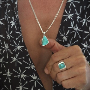 May include: A silver chain necklace with a turquoise pendant and a silver ring with a turquoise stone. The ring is on a person's finger.