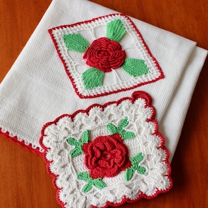 May include: Two white cotton towels with red crochet trim. Each towel features a square crochet applique with a red rose and green leaves. The appliques are centered on the towels, showcasing the handmade floral design.