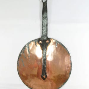 Peut inclure: Une poêle en cuivre vintage avec une longue poignée en métal foncé et une surface de cuisson circulaire. La poêle a une texture martelée et une patine foncée sur les bords. La poignée a une boucle pour suspendre.