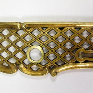 Puede incluir: Una placa de puerta de metal dorado con un patrón decorativo de rejilla de diamantes. La placa tiene una cerradura y un agujero redondo.
