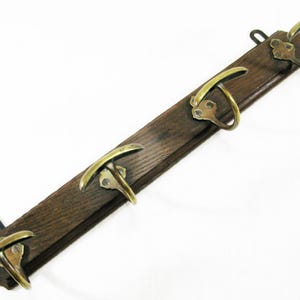 May include: A vintage wooden coat rack with four brass hooks. The dark brown wood is rectangular, with the brass hooks evenly spaced along its length. The hooks have a curved design, adding a touch of elegance.