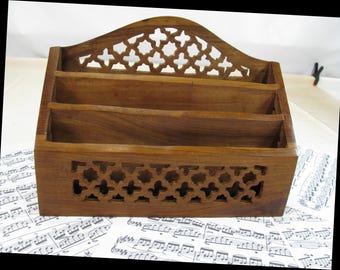May include: A brown wooden letter holder featuring three tiered compartments for organization. The front panel and the arched back panel are decorated with a repeating geometric cutout pattern. The wood grain is visible throughout the structure.