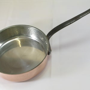 May include: A copper saucepan with a black iron handle. The saucepan has a shiny, smooth interior.