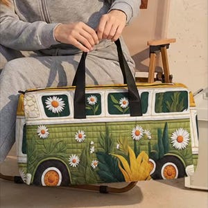 Könnte beinhalten: Eine rechteckige Reisetasche mit einem gesteppten grünen Bus-Motiv, verziert mit weißen Gänseblümchen und großen gelben Sonnenblumen. Die Tasche verfügt über schwarze Stoffgriffe und einen Reißverschluss an der Oberkante mit einem detaillierten Grafikdruck.