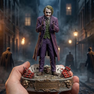 May include: A detailed figurine of the Joker in a purple suit, standing on a base with playing cards and dynamite. The base reads "AGENT OF CHAOS." The background depicts a dark alley with figures and streetlights, creating a cinematic scene.