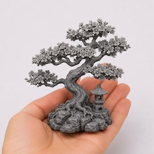 Peut inclure: Une sculpture miniature d'un bonsaï gris avec une pagode. L'arbre a un tronc tordu, des branches fleuries et repose sur une base rocheuse. La pagode est à côté de l'arbre. La sculpture est tenue dans une main.