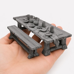 May include: Miniature gray wooden dining table set with a bench, jugs, bowls, and a horn. The table has a rustic design with a faux fur runner. The set is held in a hand, showcasing its small size.