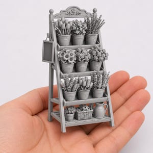 May include: A miniature gray display stand featuring three tiered shelves filled with various potted flowers, including tulips, lavender, and sunflowers. A small rectangular sign hangs from the side, and a pitcher sits on the bottom shelf.