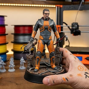 Puede incluir: Figura detallada de un personaje del videojuego Half-Life, con un traje naranja y negro, sosteniendo una palanca y un arma. La figura está sobre una base detallada. Suministros de pintura y una impresora 3D en el fondo.