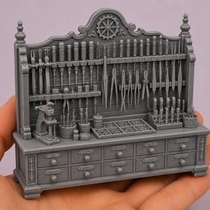 May include: A miniature gray workbench featuring a backboard with various hanging tools, including pliers and screwdrivers. The base has ten drawers labeled with text such as PINS, SCREWS, WASHERS, GLASS, SPRINGS, ARBOURS, JEWELS, BALANCE, LEVERS, and HANDS.