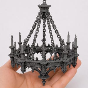 May include: A miniature gray resin chandelier featuring a circular frame with intricate gothic-style arches, pointed finials, and multiple candle-shaped holders. The structure is suspended by several linked chains meeting at a central top ring.