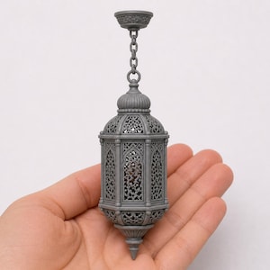 May include: A gray, ornate lantern with intricate cut-out patterns, suspended by a chain. The lantern has a domed top and a pointed base. The design is reminiscent of Middle Eastern or Moroccan style lighting.