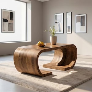 May include: A low coffee table crafted from solid wood with a continuous, curved C-shaped design. The table features a smooth, natural wood grain finish and a rectangular top surface. A small bowl containing three yellow lemons sits on the table.