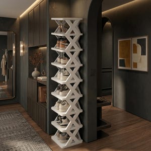 Pode incluir: Um sapateira branca de vários níveis com um design em forma de X. A sapateira está cheia de sapatos. A sapateira está colocada num corredor com paredes escuras e chão de madeira. Um espelho e obras de arte são visíveis no fundo.