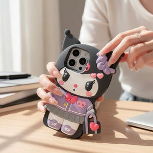 Pode incluir: Uma capa de telefone preta e branca com um personagem de desenho animado com laço, jaqueta e saia roxos. A capa tem uma bolsa em forma de coração e é segurada por uma pessoa. A capa é projetada para um smartphone.