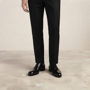 May include: A pair of black leather oxford shoes with a polished finish, featuring thin black laces and a rounded toe, worn with tailored black trousers that have a clean, straight-leg cut and a visible hem at the bottom of the pant legs.