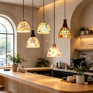 May include: Five hanging pendant lights with dome-shaped shades featuring colourful mosaic glass patterns in various designs, including floral motifs and geometric squares, suspended by thin black cords from a ceiling fixture in a room.