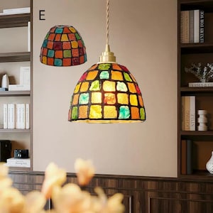 May include: A pendant light fixture featuring a dome-shaped shade constructed from a grid of multicolored glass tiles in shades of red, orange, yellow, green, and blue. The lamp is suspended by a twisted cord from a brass-toned metal fixture.