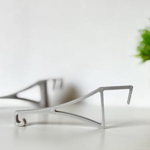 Könnte beinhalten: Zwei graue Metall-Regalhalterungen werden vor einem weißen Hintergrund gezeigt. Die Halterungen haben ein dreieckiges Design mit einem Haken an einem Ende und einer flachen Oberfläche am anderen. Die Halterungen sind zur Unterstützung von Regalen konzipiert.