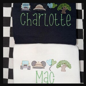May include: Two embroidered baby blankets, one navy blue and one white. The navy blanket has the name "Charlotte" in green script, with embroidered safari-themed images. The white blanket has the name "Mac" in green script, with similar safari-themed images.