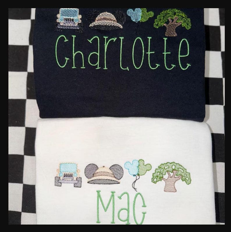 May include: Two embroidered baby blankets, one navy blue and one white. The navy blanket has the name "Charlotte" in green script, with embroidered safari-themed images. The white blanket has the name "Mac" in green script, with similar safari-themed images.