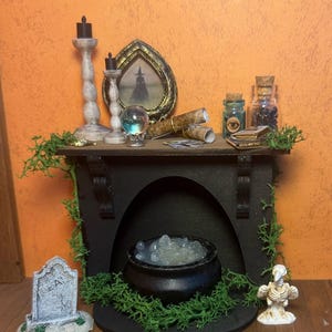May include: A miniature black fireplace mantel featuring a cauldron filled with translucent white liquid, two black candles, a framed silhouette of a witch, a crystal ball, rolled scrolls, glass bottles, a tombstone, and a bird skeleton.