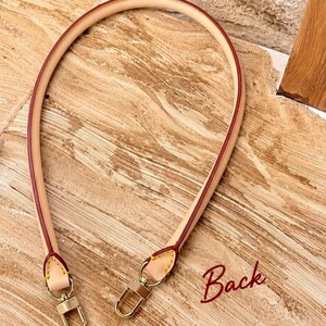 Pu&ograve; includere: Una tracolla per borsa in pelle beige con bordi dipinti in rosso e cuciture gialle. La cinghia presenta due chiusure a moschettone in metallo dorato alle estremit&agrave;. La parola Back &egrave; scritta in corsivo rosso in basso a destra.
