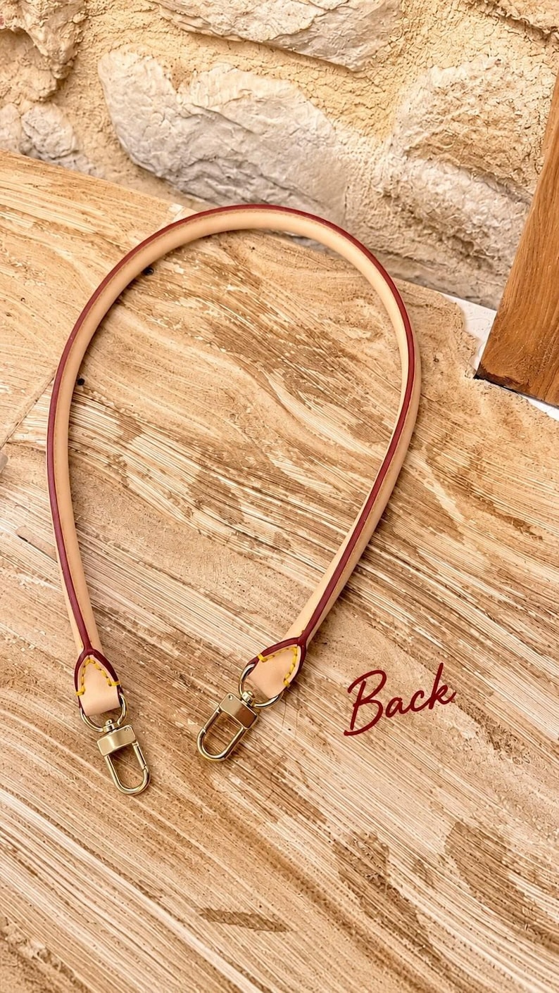Pu&ograve; includere: Una tracolla per borsa in pelle beige con bordi dipinti in rosso e cuciture gialle. La cinghia presenta due chiusure a moschettone in metallo dorato alle estremit&agrave;. La parola Back &egrave; scritta in corsivo rosso in basso a destra.