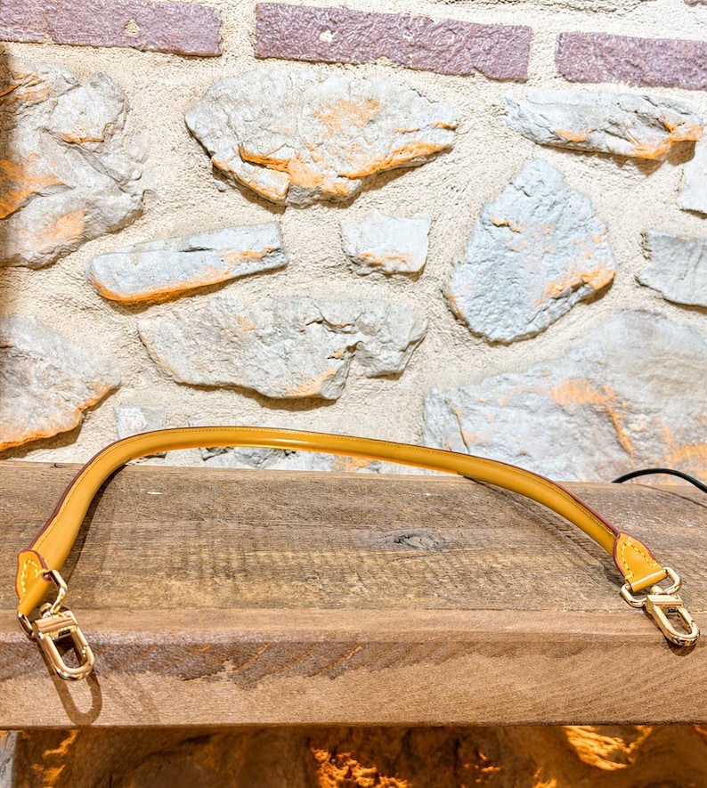 Pu&ograve; includere: Una tracolla per borsa color giallo senape con bordi lisci e arrotondati, dotata di chiusure a moschettone in metallo dorato su entrambe le estremit&agrave;. Il cinturino presenta cuciture visibili nei punti di attacco per un fissaggio sicuro.