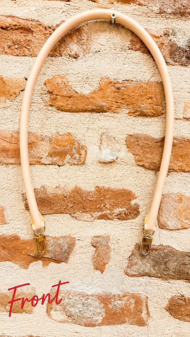 Pu&ograve; includere: Una tracolla per borsa in pelle beige chiaro, arrotondata, dotata di chiusure a moschettone in metallo dorato su entrambe le estremit&agrave;. La tracolla &egrave; arcuata a semicerchio. La parola Front &egrave; scritta in corsivo rosso in basso a sinistra.