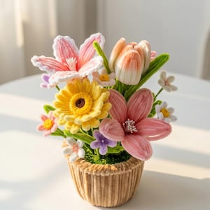 May include: A handmade floral display in a small, corduroy-textured pot. The bouquet includes crocheted flowers in pink, yellow, and white, with green stems and leaves. The arrangement is a delightful decorative item, perfect for a home.