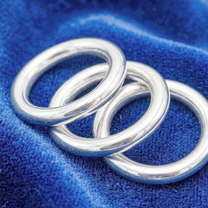 May include: Three polished silver-toned metal rings with a smooth, rounded surface. The rings are arranged in a slightly overlapping, diagonal formation, showcasing a reflective, metallic finish on each circular band.