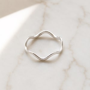 Puede incluir: Un anillo de plata pulida que presenta un diseño de banda ondulada y sinuosa continua. La superficie metálica es lisa y reflectante, mostrando un brillo metálico constante en toda la estructura circular de la pieza de joyería.