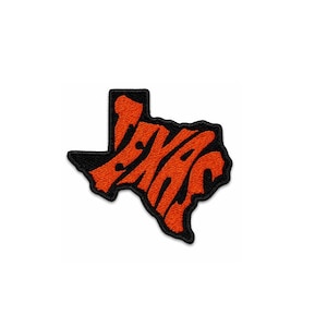 Può includere: Toppa ricamata arancione e nera a forma di stato del Texas. La parola "TEXAS" è scritta in un font stilizzato all'interno del contorno dello stato. La toppa ha un bordo nero ed è posta su uno sfondo bianco.