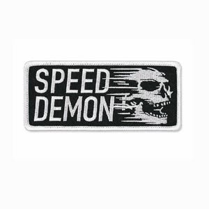 May include: A rectangular patch with a black border and white background. The patch features the words "SPEED DEMON" in a bold, sans-serif font above a stylized skull graphic with speed lines.