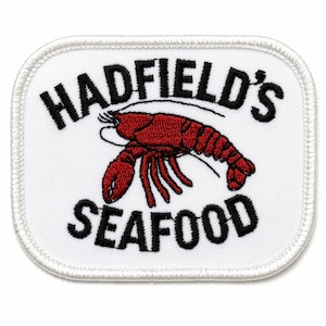 May include: White, rectangular patch with rounded corners. The patch features the text "HADFIELD'S SEAFOOD" in black, arched above and below a red lobster illustration. The patch has a white border.