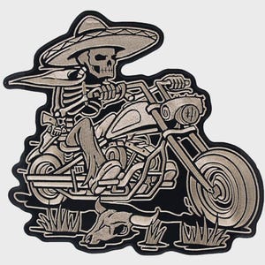 May include: Embroidered patch featuring a skeleton wearing a sombrero riding a motorcycle. The design includes a skull, motorcycle details, and a desert scene with a skull and grass. The patch has a black border and is in shades of gray.