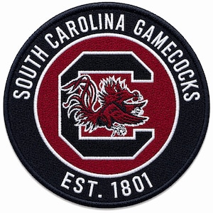 May include: Circular patch with the text "SOUTH CAROLINA GAMECOCKS" in white lettering on a navy blue background. The center features a red and black logo with a stylized rooster and the text "EST. 1801".