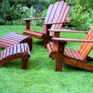 Könnte beinhalten: Zwei Adirondack-Stühle aus Holz und zwei passende Fußstützen stehen auf einem grünen Rasen. Die Stühle haben breite Armlehnen und Lattenrücken. Die Fußstützen sind gebogen und ebenfalls aus Holz.