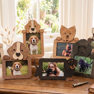 May include: A collection of wooden picture frames shaped like various dog breeds, including a golden retriever, beagle, yorkshire terrier, poodle, and french bulldog. Each frame features a cutout of a dog head or body holding a rectangular photo insert.