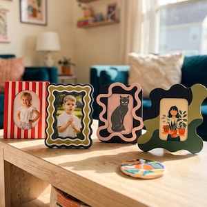 May include: Four rectangular picture frames with distinct designs: one with red and white vertical stripes, one with a wavy green and black border, one with a wavy pink and black border, and one with an irregular green and black camouflage pattern.