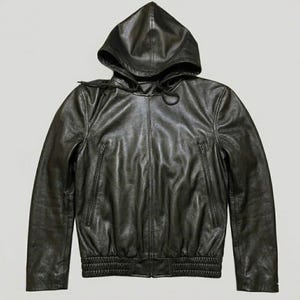 May include: Black leather hooded jacket with a zip-up front and two side pockets. The jacket features a drawstring hood and ribbed cuffs and hem. The leather has a slightly wrinkled texture.