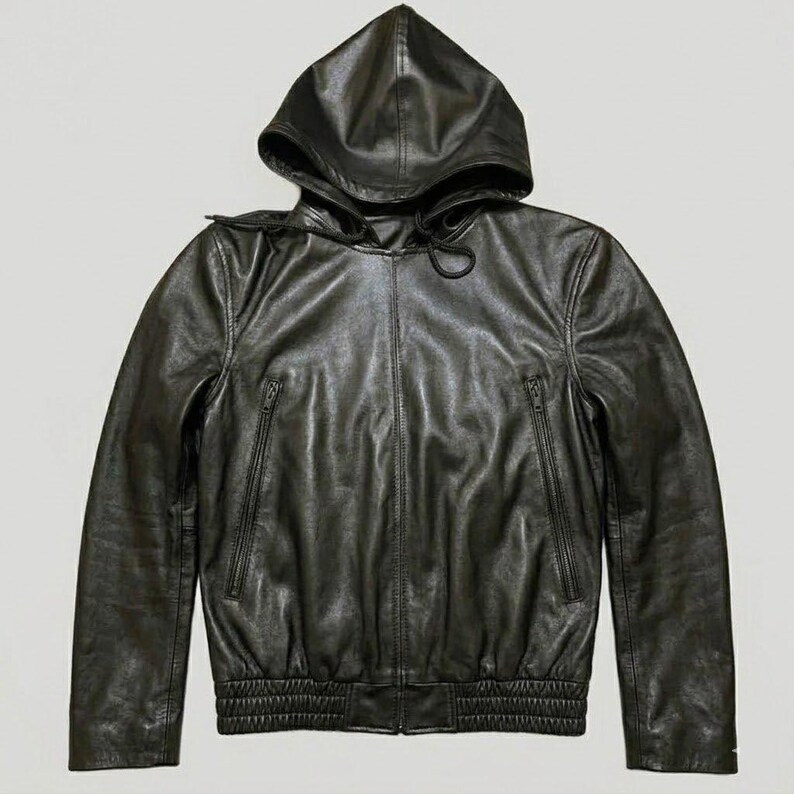 May include: Black leather hooded jacket with a zip-up front and two side pockets. The jacket features a drawstring hood and ribbed cuffs and hem. The leather has a slightly wrinkled texture.