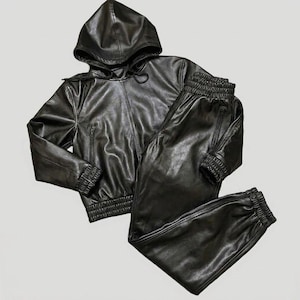May include: A black faux leather tracksuit set. The set includes a hooded jacket with a zipper closure and matching pants with elastic cuffs and a drawstring. The jacket has a hood and the pants have pockets. The material has a shiny appearance.