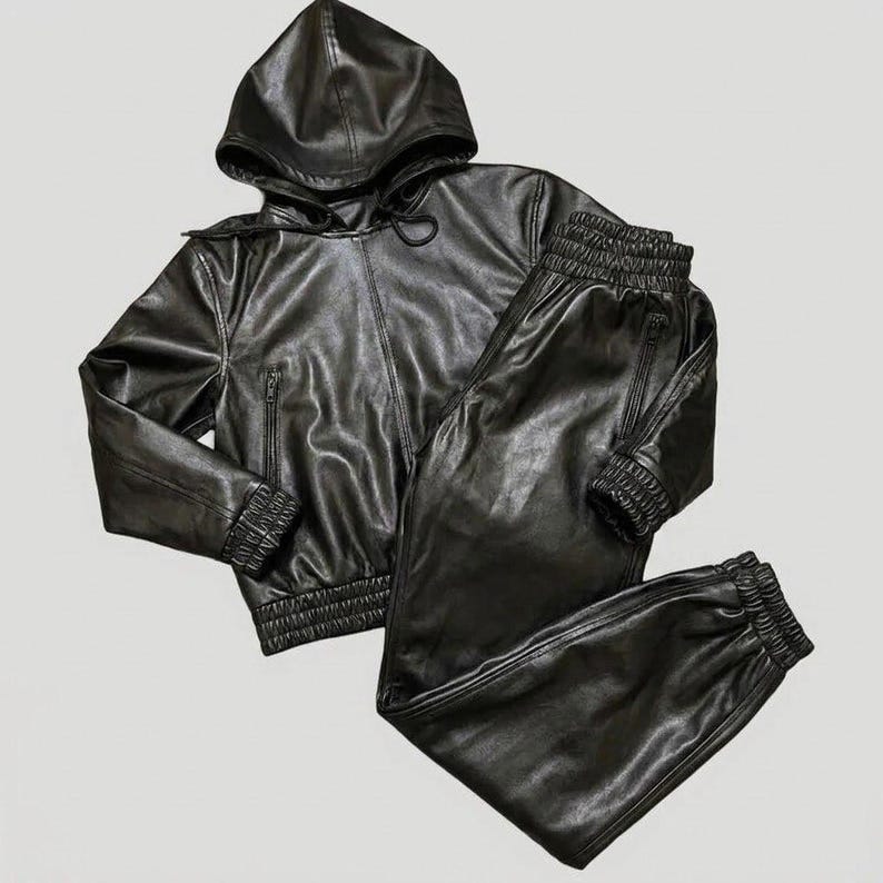 May include: A black faux leather tracksuit set. The set includes a hooded jacket with a zipper closure and matching pants with elastic cuffs and a drawstring. The jacket has a hood and the pants have pockets. The material has a shiny appearance.