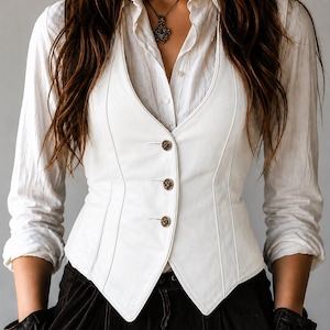 May include: A white leather vest with three decorative buttons. The vest is worn over a white button-down shirt. The image also shows a black necklace and black gloves. The vest has a tailored fit and a V-neck design.