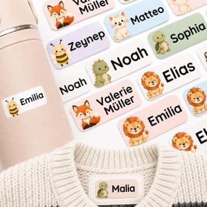 Könnte beinhalten: Eine Sammlung rechteckiger Klebeetiketten mit verschiedenen Zeichentricktieren wie Füchsen, Katzen, Bienen, Schildkröten, Löwen und Dinosauriern. Jedes Etikett zeigt einen Namen in schwarzer Schrift und ist auf einer rosa Flasche und einem Pullover.