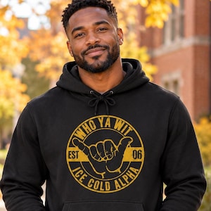 May include: A black hooded sweatshirt featuring a gold circular graphic on the chest. The design includes a hand making a shaka gesture, the text WHO YA WIT, EST 06, and ICE COLD ALPHA. The hoodie has long sleeves and a front kangaroo pocket.