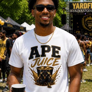 May include: A white short-sleeve t-shirt featuring the text APE JUICE in black and gold lettering above a graphic of a golden ape figure emerging from a bucket with gold liquid splashes. The shirt is worn with a gold chain and black shorts.