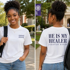 May include: A white short-sleeve t-shirt featuring the text JEHOVAH JEHOVAH printed in navy blue on the front left chest. The back of the shirt displays the text HE IS MY HEALER in large navy blue letters with JEHOVAH RAPHA printed below it.
